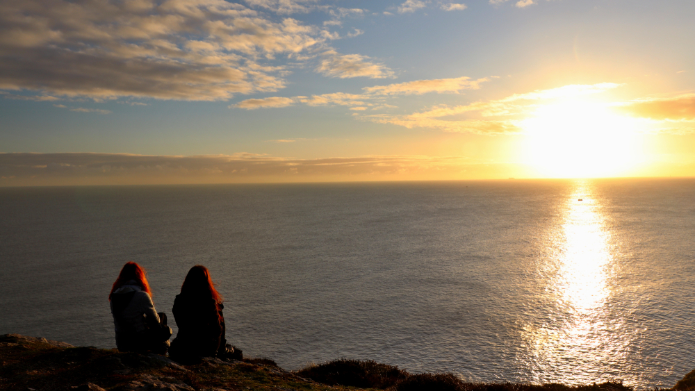 Two friends sitting by the sea watching the sunrise in Howth, Ireland