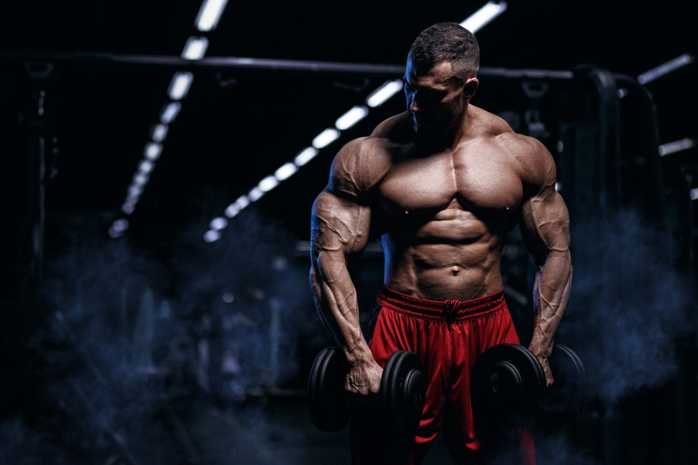 Muscular man bodybuilder training in gym and posing