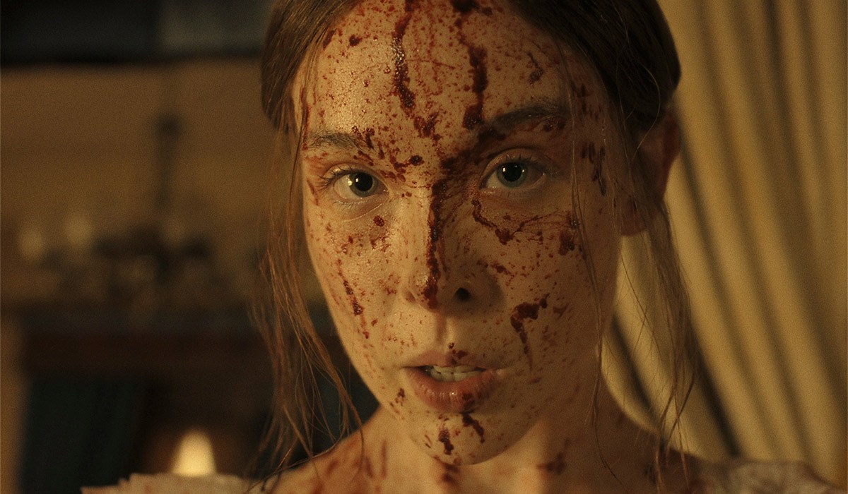 Dark and twisted new chapter of Monster series lands on Netflix 7 "A young woman with long hair, dressed in light clothing, has her face and upper chest covered in blood, standing indoors with dim warm lighting and blurred curtains and furnishings in the background."
